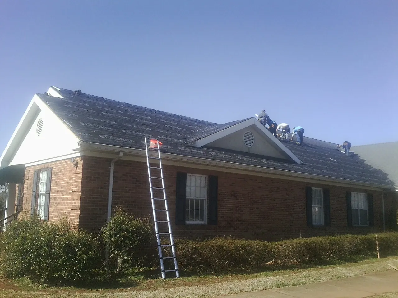 Crew tearing shingles off a brick ranch roof with a ladder set — Emergency Roof Repair work by our crew in Dungannon