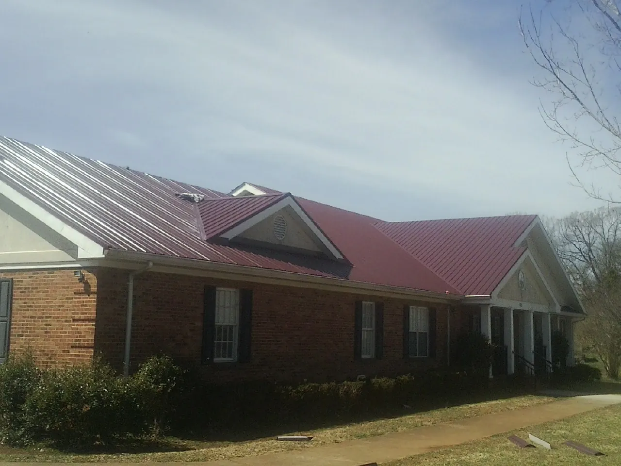 Red metal roof with gabled entries on a long brick building, from a Hail Damage Roof Repair job in Dungannon