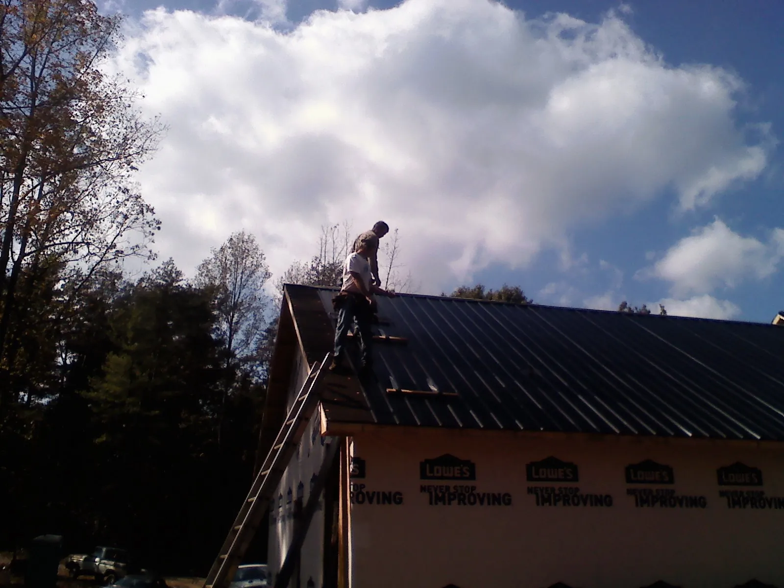 Roofer fastening dark metal panels high against a cloudy sky, from a Roof Inspection job in Dungannon